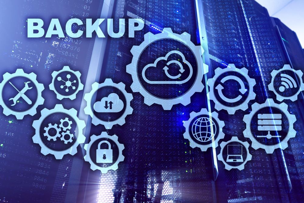 A conceptual graphic of IT servers and gears with cloud graphics, laptops, security icons and more signifying backup and business continuity.