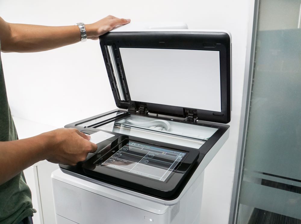 A person using an office copier with a touchscreen interface, scanning a document in a modern workplace setting.