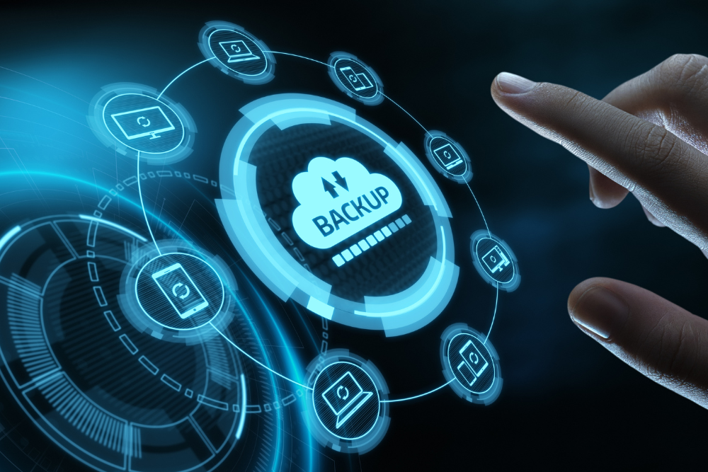 Conceptual image of a backup continuity plan a large hand attempts to press a backup button with icons of laptops, tablets, cell phones and more around it.